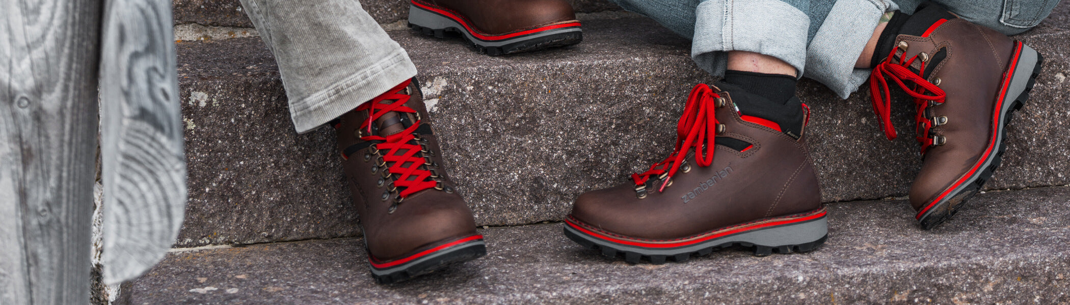 Two people sitting on cement steps wearing Zamberlan Solden GTX and Toblach GTX hiking and lifestyle boots. 